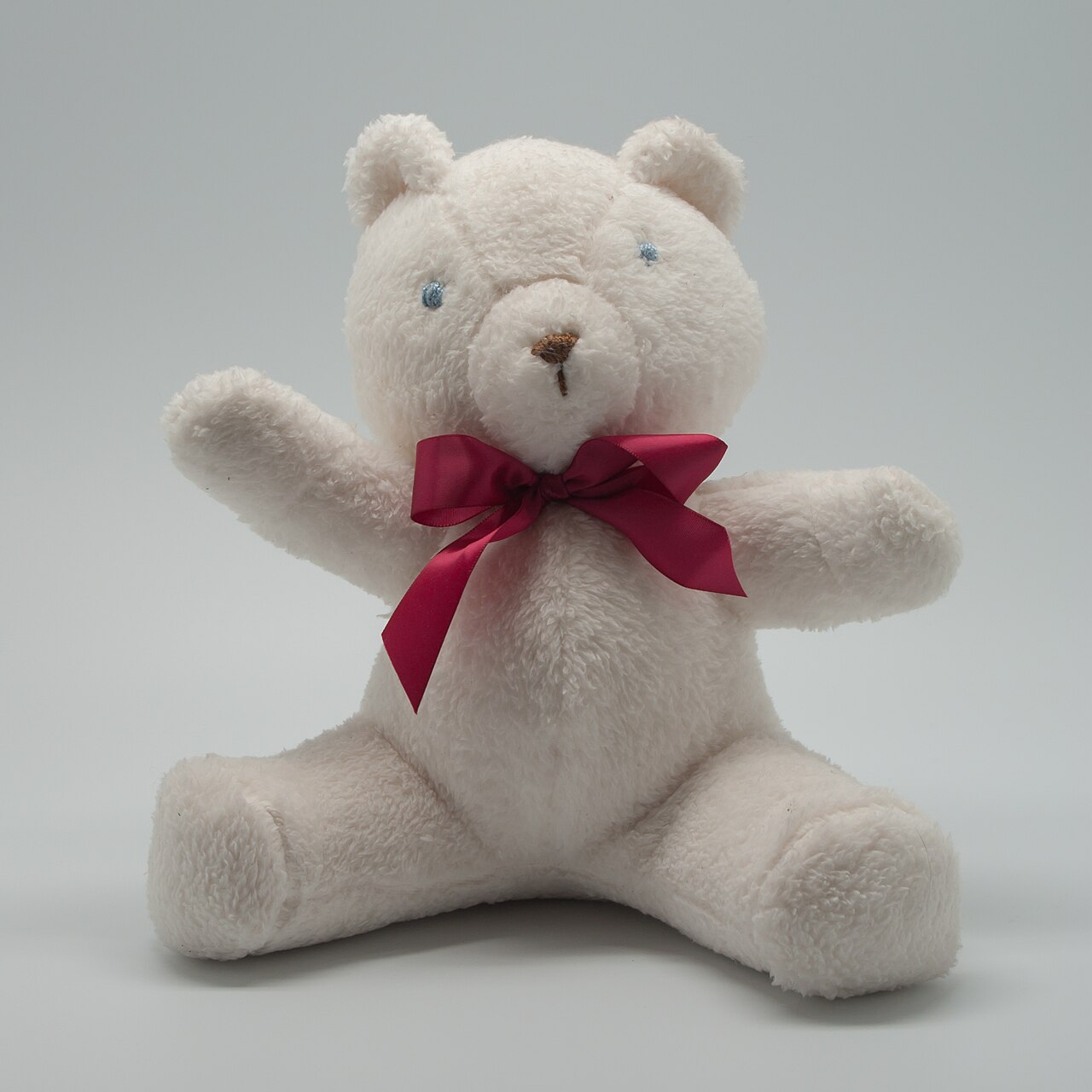 Handgemaakte teddybeer met gestikte naden, zittend tegen een lichte achtergrond
