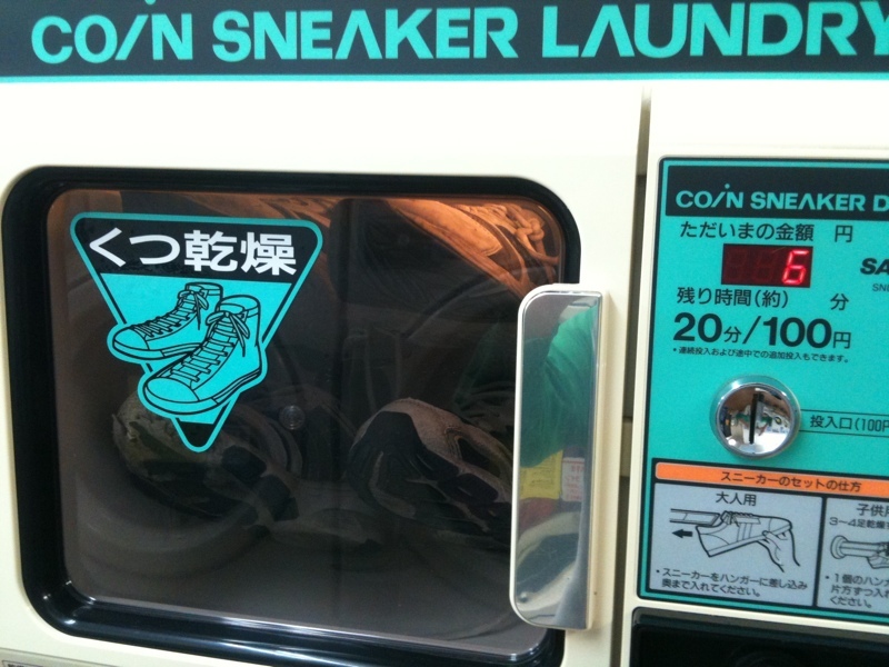 Muntautomaat voor het drogen van schoenen in een Japans wassalon, met een sticker van twee sneakers op het venster