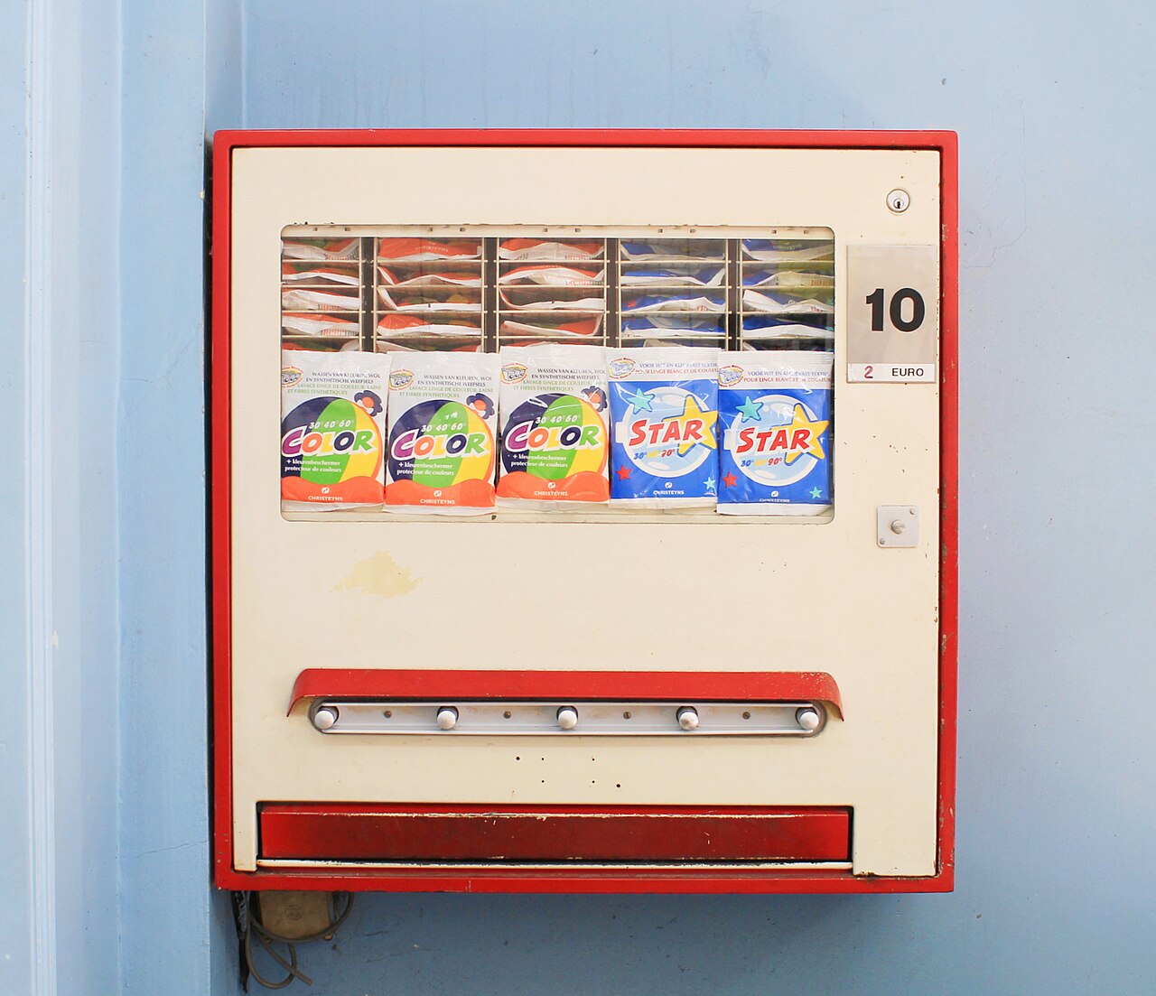 Oude wasmiddelautomaat aan de muur van een Belgisch wassalon, met zakjes waspoeder achter glas